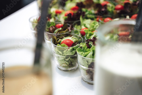 Rows of glasses with vegetable salad. Lettuce, tomato and sliced cucumber in glass. Celebration, party, birthday or wedding concept.