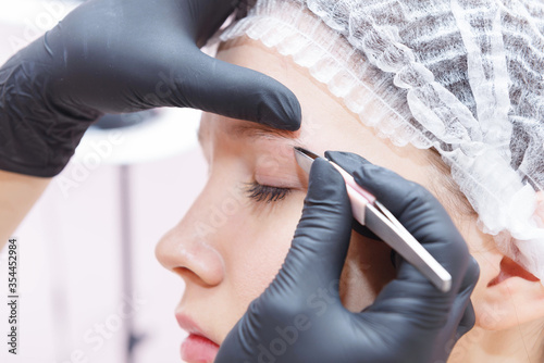 The master removes tweezers with eyebrow hair after the procedure.