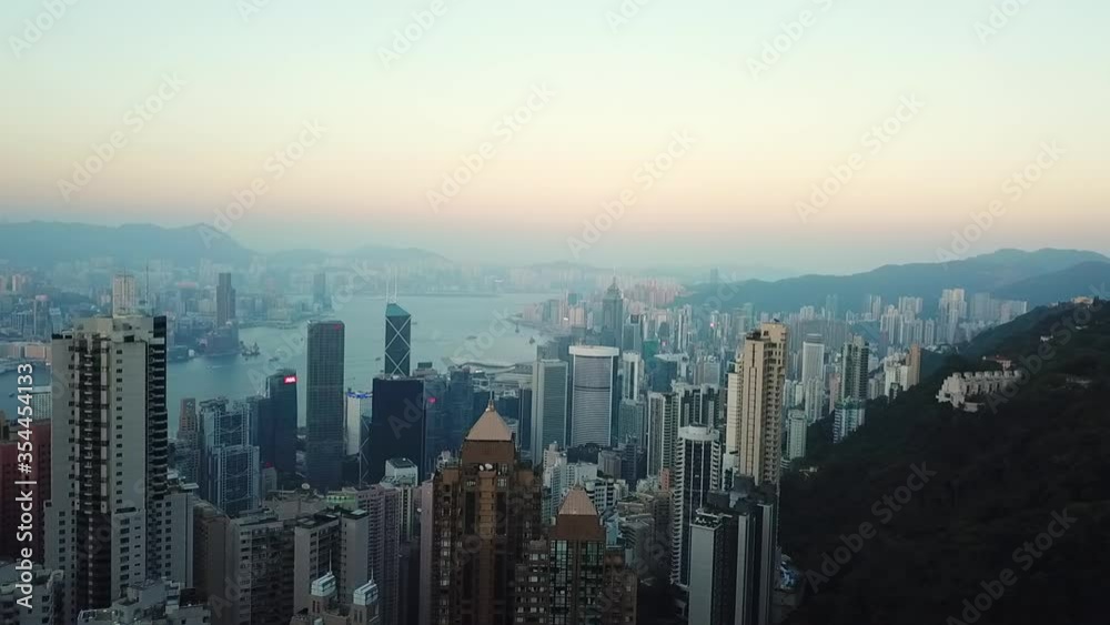Aerial panning shot of cityscape by mountains and sea against sky, drone flying over modern buildings in city at sunset - Hong Kong, China Aerial panning shot of cityscape by mountains and sea against sky, drone flying over modern buildings in city at sunset - Hong Kong, China