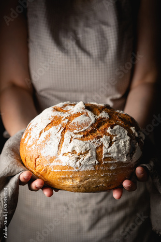 Female hands holding loaf of homemade rye bread with cracks and flour on towel. Concept for bakery poster or cover