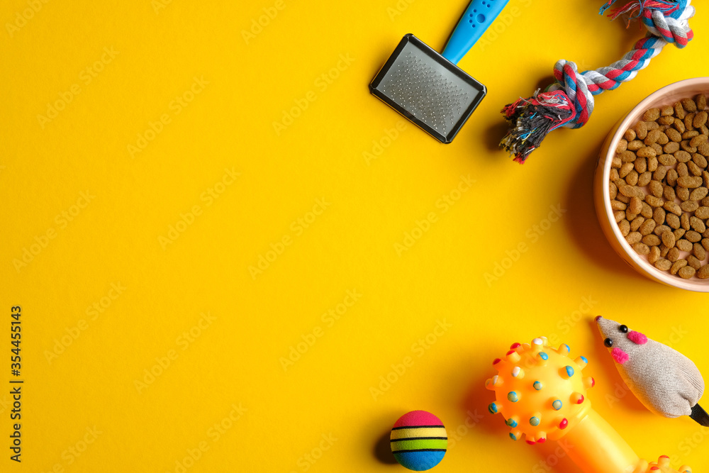 Pet care and training concept. Flat lay composition with toys for cat and dog and bowl with dry food on yellow background.