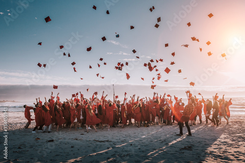 high school of college class of 2020 in a silhouette of people jumping on the beach tossing their caps or hats in the air in celebration of graduation.