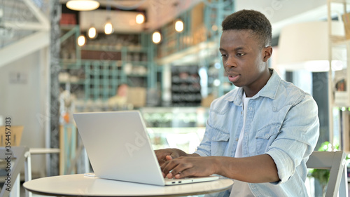 Cheerful Young African Man Working on Laptop in Cafe
