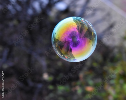 Colorful large floating bubble, out of focus grey trees in background, cityscape reflected in bubble