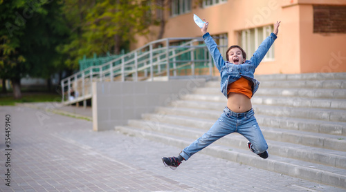 Happy boy jumps in schoolyard holding protective mask in the hand. Emotional kid jumping. Happyness of the end of pandemic 2020