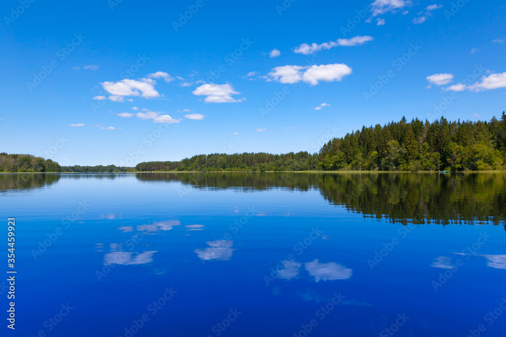 Blue lake and blue sky with reflections of white clouds in the water. In the background forest. Seliger Lake in Russia.