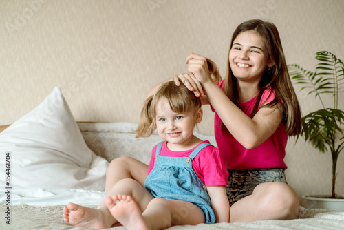 Children play on the bed in a bright bedroom. teen girl combing baby hair. funny girls. sisterly love. vacation home.