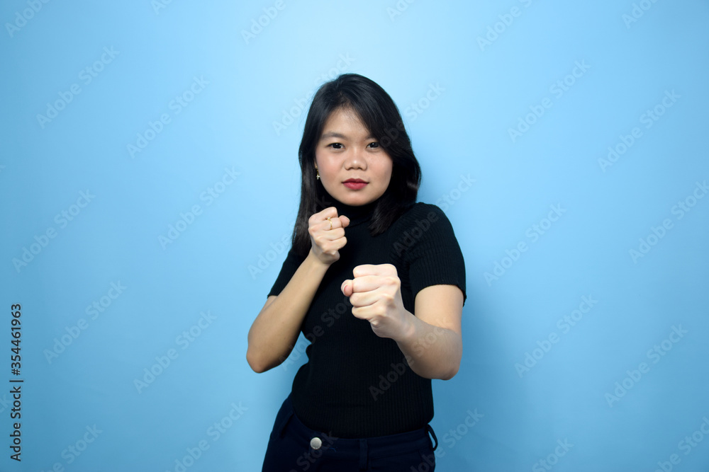 Fototapeta premium Portrait of Young beautiful asian women wearing black turtle neck shirt with blue isolated background, Punching fist to fight, Fight Gesture Concept