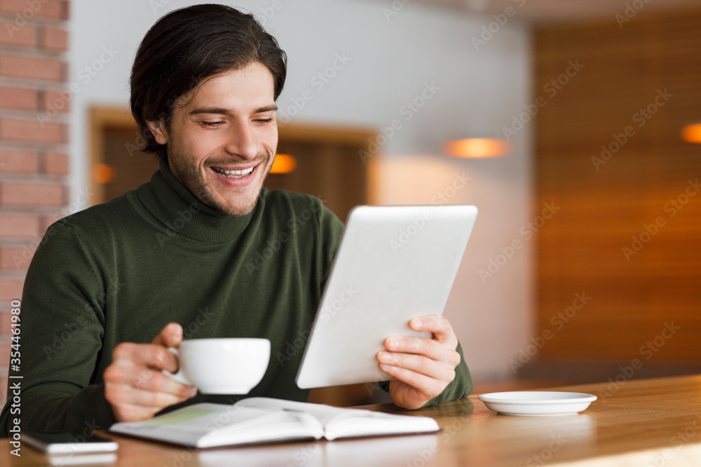 Freelancer having morning coffee at cafe, checking news on tablet Freelancer having morning coffee at cafe, checking news on tablet