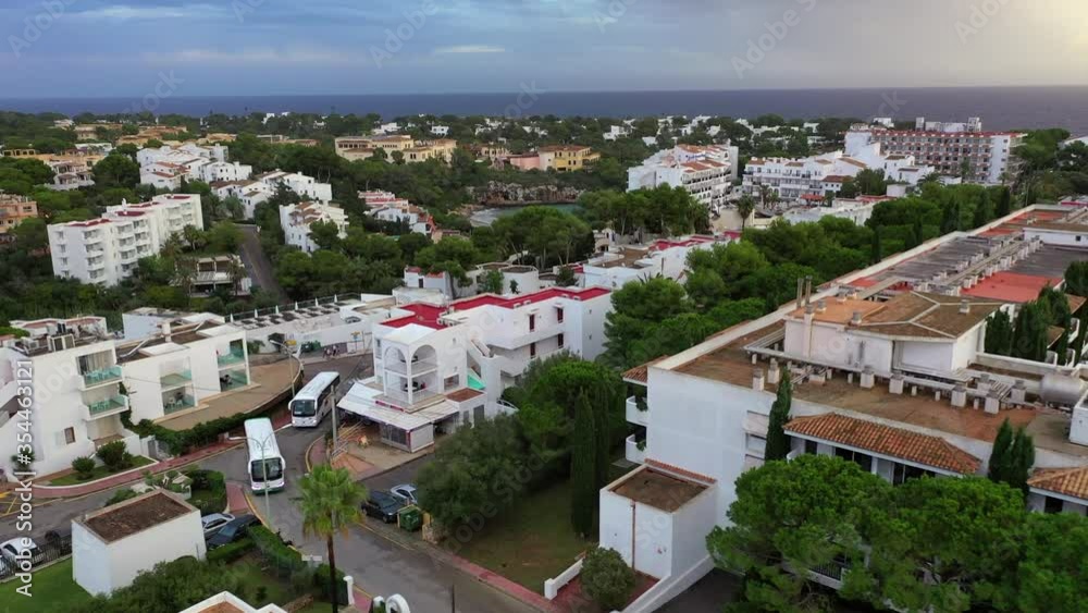 Aerial shot of buildings in city against cloudy sky at morning, drone ascending backward from sea - Cales de Mallorca, Spain Aerial shot of buildings in city against cloudy sky at morning, drone ascending backward from sea - Cales de Mallorca, Spain