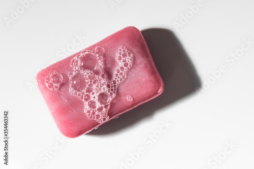 Classic pink bar of soap with bubbles shot from above top down on a clean white seamless surface.