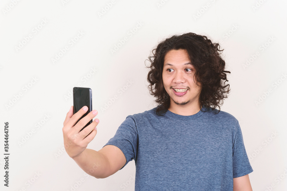 Portrait of Asian man smiling and holding mobile phone for selfie, video call or playing social media Portrait of Asian man smiling and holding mobile phone for selfie, video call or playing social media