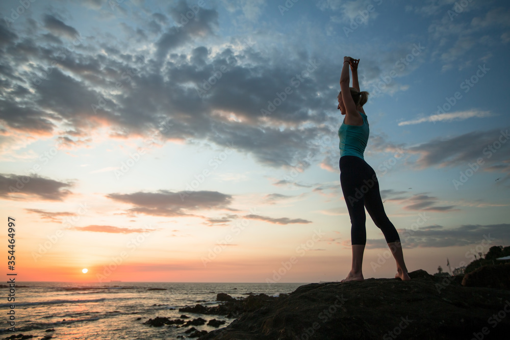 A young woman practicing yoga during sunset on the seashore.