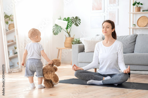Young mom practicing yoga at home, meditating next to baby
