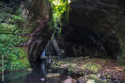 Gruta e cachoeira das Andorinhas - Rolante - RS. Beautiful natural setting of a cave and waterfall with sunbeams. Swallows waterfall – Rolante - Rio Grande do Sul – Brazil
