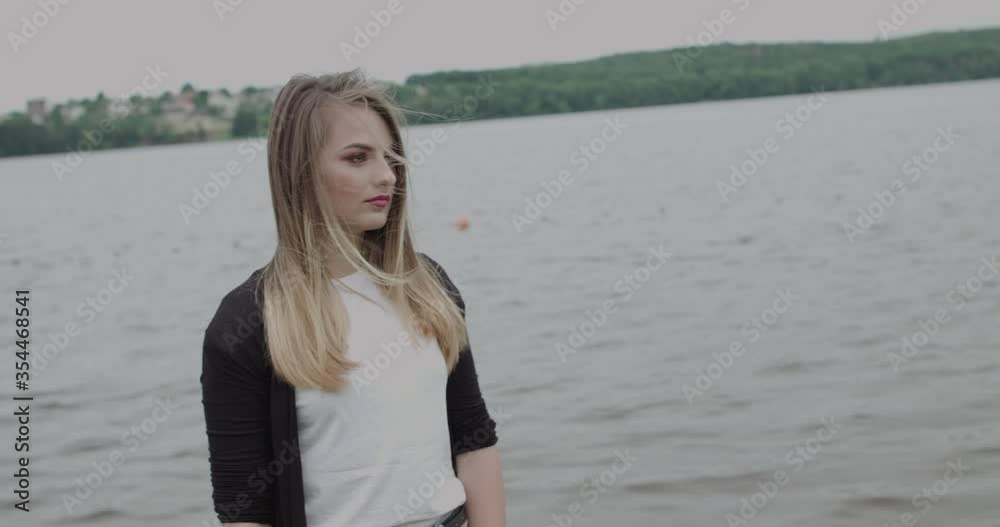 Pretty girl with blowing hair looking far and turning at camera at river Pretty girl with blowing hair looking far and turning at camera at river