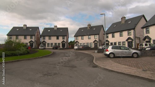 Panning shot of vehicles parked by houses in town against cloudy sky - Galway, Ireland photo