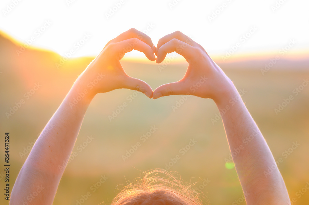Hands making heart shape with sunset. Close up of woman hands making heart shape gesture. High quality photo .