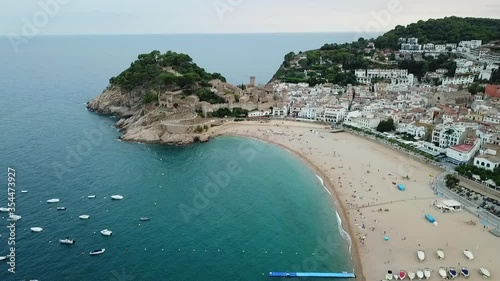 Aerial shot of people at beach by famous historic castle, drone flying forward towards fort in city by sea against sky - Tossa de Mar, Spain photo