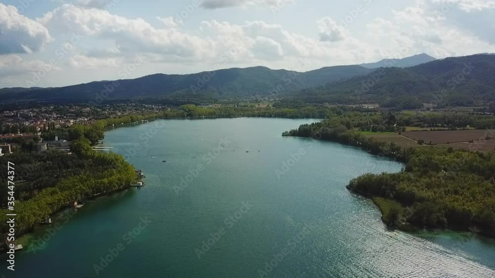 Aerial shot of lake near city and mountains against sky, drone flying backward on sunny day - Lake of Banyoles, Spain Aerial shot of lake near city and mountains against sky, drone flying backward on sunny day - Lake of Banyoles, Spain