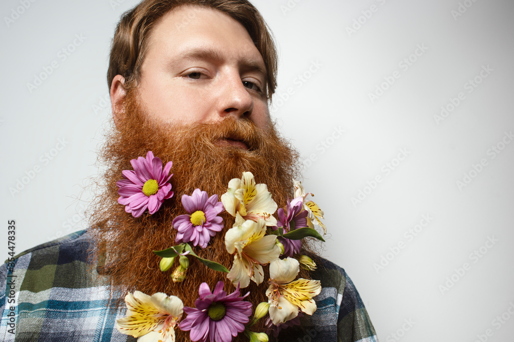 A man with a beautiful red hair and a red beard on the gray background. A bearded man with a decorated beard for the holiday. Flower in the beard. A man with a beautiful red hair and a red beard on the gray background. A bearded man with a decorated beard for the holiday. Flower in the beard.
