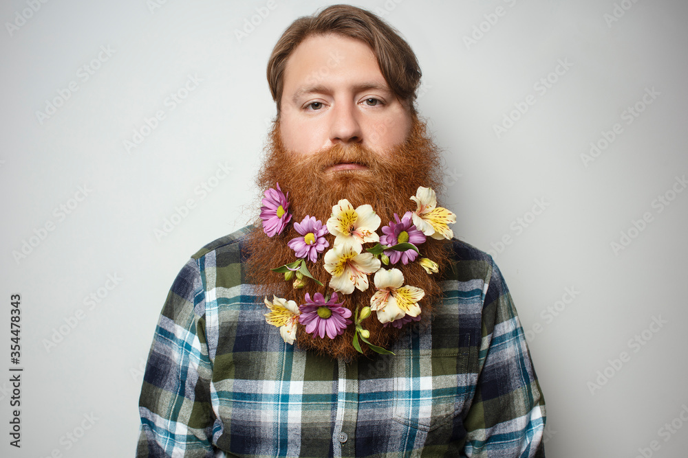 A man with a beautiful red hair and a red beard on the gray background. A bearded man with a decorated beard for the holiday. Flower in the beard. A man with a beautiful red hair and a red beard on the gray background. A bearded man with a decorated beard for the holiday. Flower in the beard.