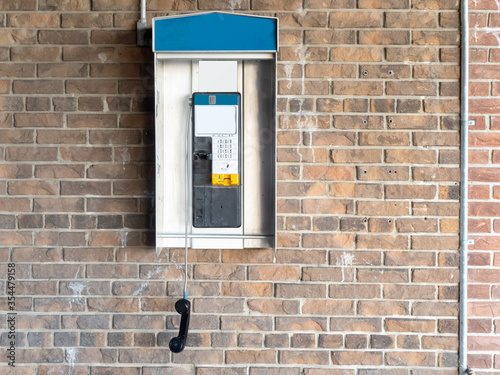 Bild auf Leinwand a classic pay phone on a brick wall with the receiver dangling off the hook