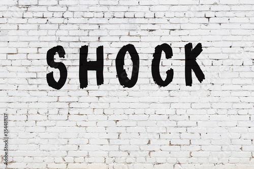 Word shock painted on white brick wall