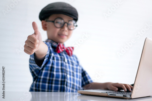 Genius boy appears a thumbs up while using a laptop computer, focus on the thumbs up © chomplearn_2001