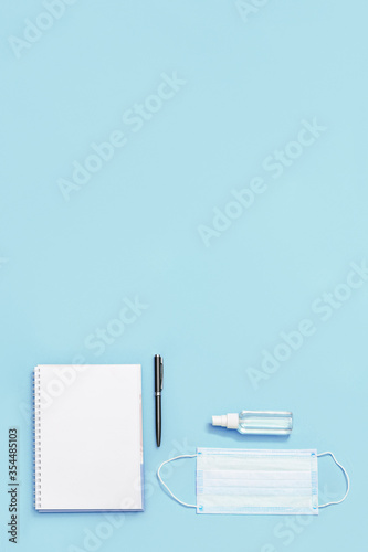 Flat lay with stationery for school, education and personal protective equipments. Face medical mask, hand sanitizer, notebook, pen. Top view and copy space.