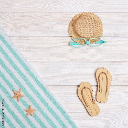 Summer composition, towel, beach slippers, hat, sunglasses on white wood, summer background with copy space. Pastel colored. Vacation by sea.