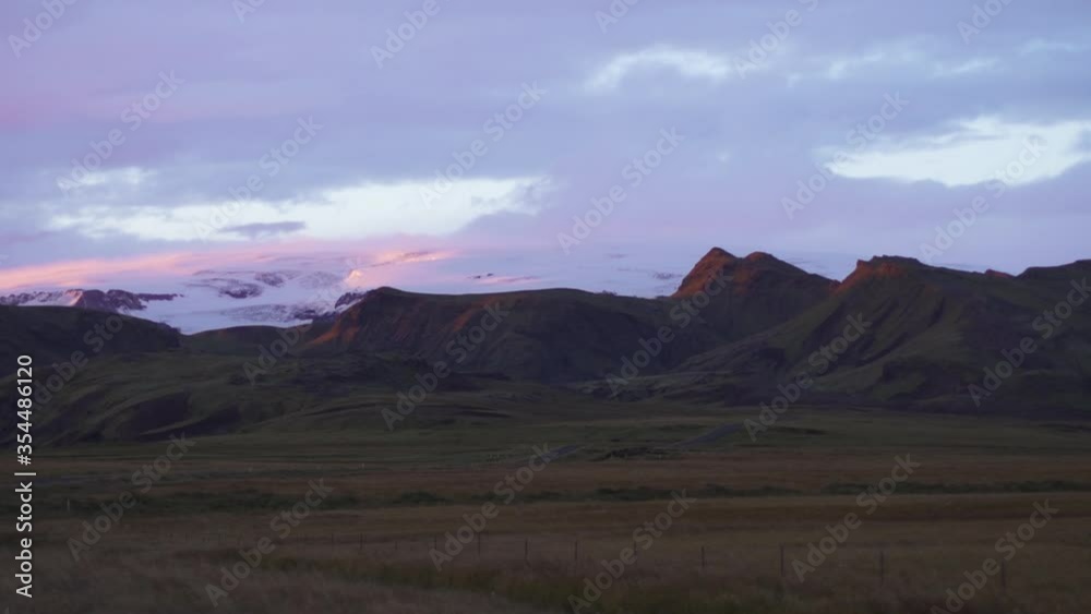 Evening blue-hour view of Icelandic landscape with blue and pick skies. Grassy fields and mountians in view, with snow and clouds in the distance. Evening blue-hour view of Icelandic landscape with blue and pick skies. Grassy fields and mountians in view, with snow and clouds in the distance.