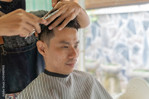 Asian young man with boy friend hairdresser trimming black hair with scissors at garden in home.