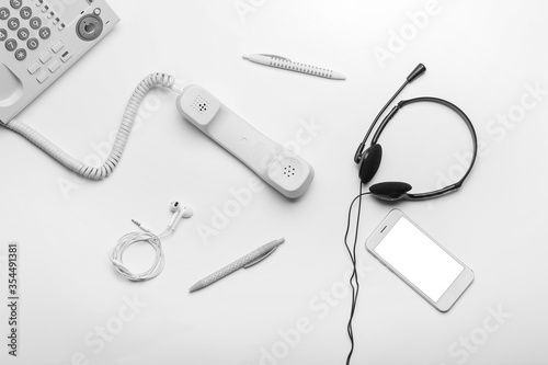 Headset, pens, earphones and telephone with mobile phone on white background