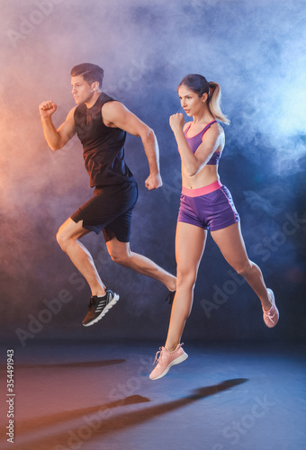 Sporty running young couple on dark background