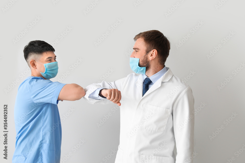 Young doctors greeting each other on light background. Concept of epidemic Young doctors greeting each other on light background. Concept of epidemic