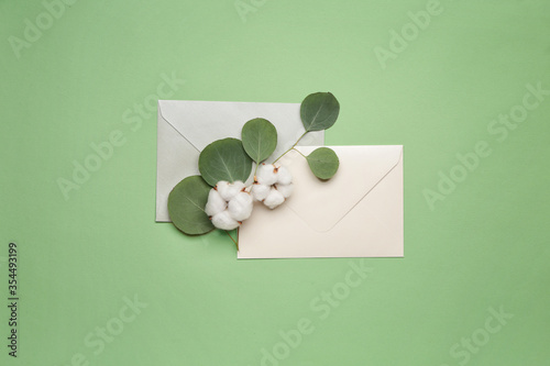 Beautiful cotton flowers, envelopes and eucalyptus leaves on color background