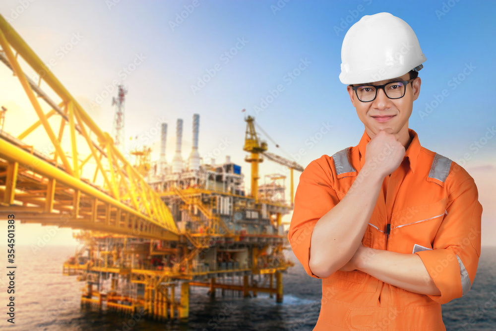 Asian confident and smart engineer man wearing coveralls suit and helmets  for safety isolated on offshore oil rig platform background. Stock Photo