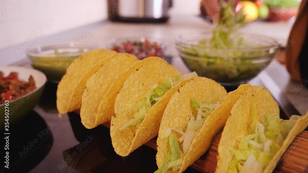 Woman hand making tacos, stuffing hard taco shells - adding the base layer of lettuce, camera orbit, close up. Phases of making tacos. Woman hand making tacos, stuffing hard taco shells - adding the base layer of lettuce, camera orbit, close up. Phases of making tacos.