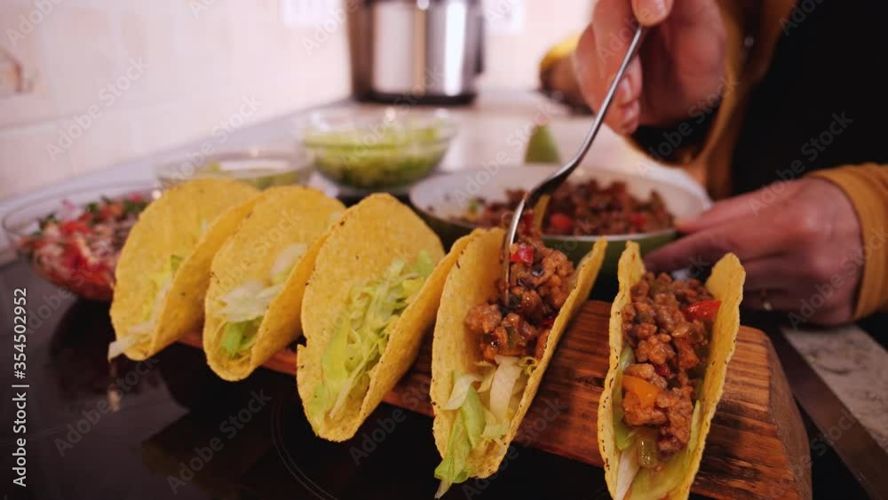 Woman hand stuffing hard taco shells - adding the ground meat and vegetables filling, camera orbit, close up. Phases of making tacos.