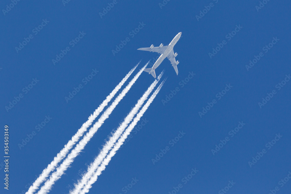 Large four engined commercial airliner jet aircraft flying at high altitude with a large contrail flowing behind it. - obrazy, fototapety, plakaty 