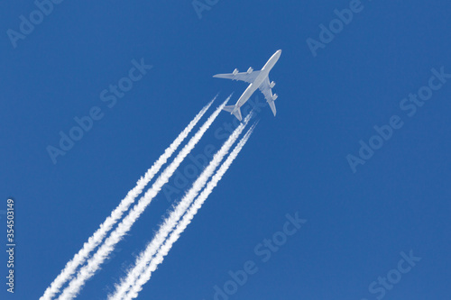 Large four engined commercial airliner jet aircraft flying at high altitude with a large contrail flowing behind it.