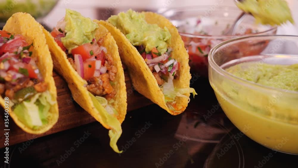 Woman hand prepare tacos - adding the guacamole topping, camera orbit, close up. Phases of making delicious taco.