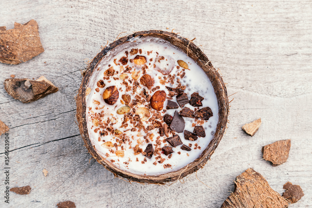  Coconut milk and granola made from oatmeal, nuts,dried fruits and grated chocolate in a coconut shell on a wooden background.Сoncept of healthy food and healthy desserts.Copy space for text