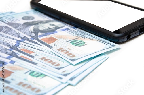 Dollars and smartphone. Banknotes in denominations of 100 dollars lie on a white background on them, next to them lies a smartphone with a white screen. Top view and angle Macro smartphone and dollars