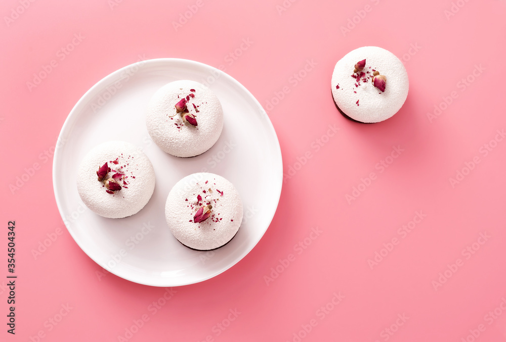Mousse pastry dessert covered with white chocolate and decorated with rose buds on pastel pink background. Modern stylish cake. Flat lay style. Copy space. Close-up.