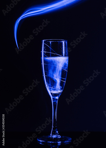 A glass of champagne on a black background with the effect of drawing blue light on a long shutter speed. Concept idea for decorating a party or holiday in neon style.