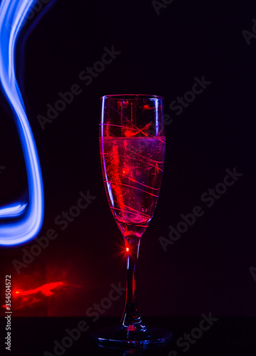 red-lit champagne glass on a black background with the effect of drawing blue light on a long shutter speed. Concept idea for decorating a party or holiday in neon style