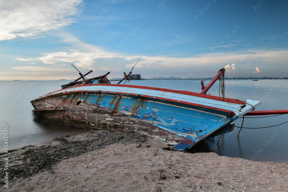 The remains of a blue fishing boat sunk on the beach are left amidst tranquility.