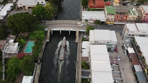 Boats moving to station for embarkation and disembarkation. Boats moving pass under the bridge. There are views along the canal ex. temple, walk way. photo